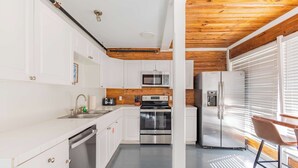 A modern kitchen with white cabinets, stainless steel appliances, and a wooden ceiling. - Commodore's Compound - One block from Duval St (Key West)