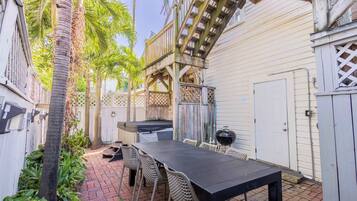 A patio with a table and chairs, a grill, and a wooden deck.