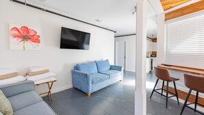En moderne stue med sofa, blå sofa, fjernsyn og træloft.