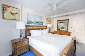 A bedroom with a bed, two nightstands, a ceiling fan, and artwork on the walls.