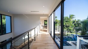 Un intérieur moderne avec un escalier en bois, de grandes fenêtres et une vue sur une piscine extérieure.