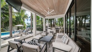 Un espace de vie extérieur moderne comprenant une piscine, des chaises longues, une table à manger et un coin cuisine.