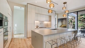 Une cuisine moderne dotée d’un grand îlot central, d’appareils électroménagers en acier inoxydable et offrant une vue sur la verdure environnante.