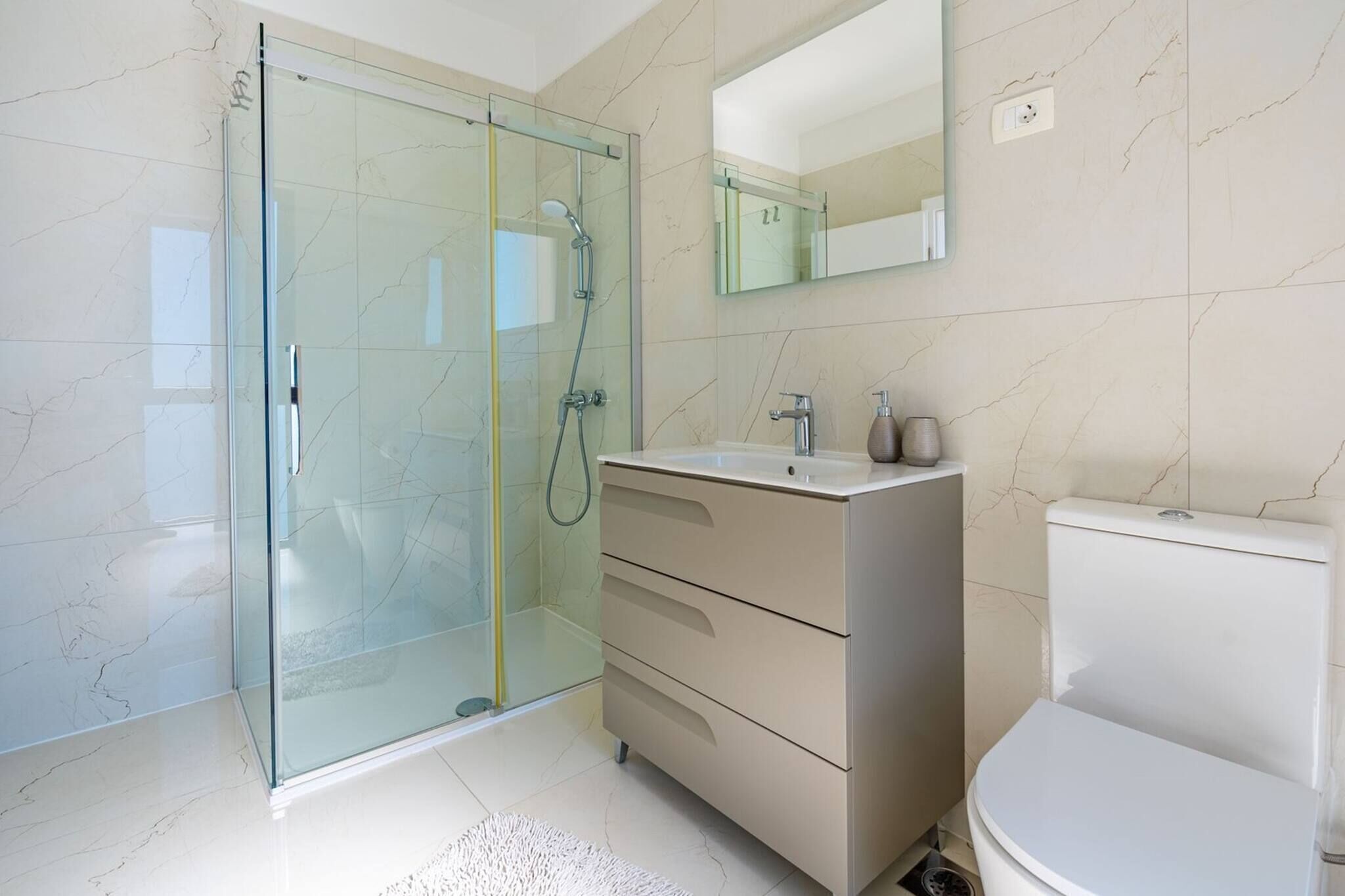 A modern bathroom with a glass-enclosed shower, a white sink, a toilet, and a mirror above the sink.