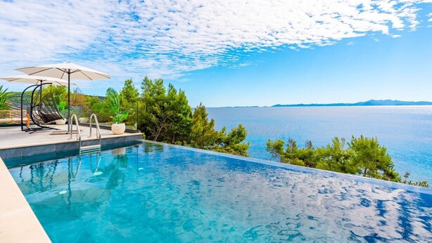 Une piscine avec vue sur la mer, entourée de verdure et sous un ciel dégagé.