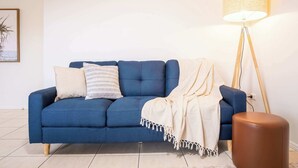 A blue sofa with a white throw blanket, a floor lamp, and a framed picture on the wall. - Saltair Kings Beach Apartment - Walk to Beach (Kings Beach)