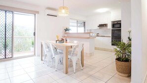 A modern kitchen with white cabinets, a wooden dining table, and a hanging light fixture. - Saltair Kings Beach Apartment - Walk to Beach (Kings Beach)