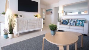 Ein modernes Wohnzimmer mit einem weißen Sofa, einem Holztisch, einem Flachbildfernseher und einem Kamin.