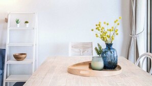 Ein moderner Essbereich mit einem hellen Tisch, weißen Stühlen, einer Vase mit gelben Blumen und einer hohen Stehlampe.