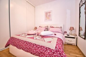 A bedroom with a bed, two bedside tables, a nightstand, a mirror, and a picture on the wall.