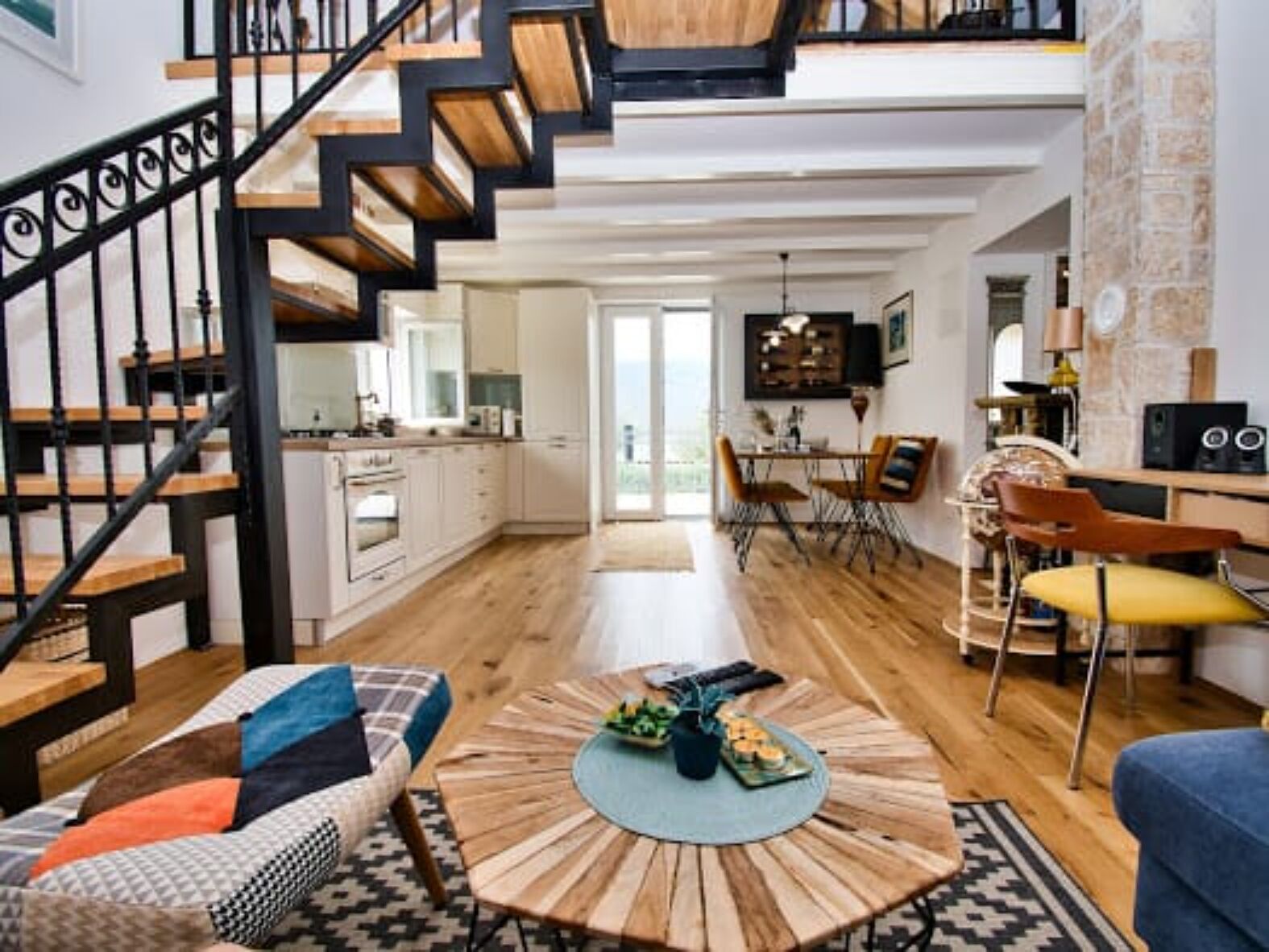 Een modern interieur met een houten trap, een eethoek met een ronde tafel, en een zithoek met een bank en salontafel.