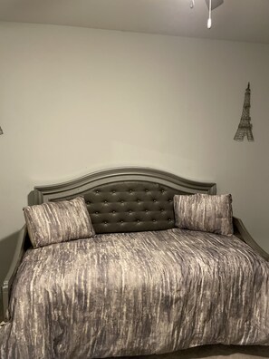 Una cama con cabecera capitonada, dos almohadas y una colcha estampada.