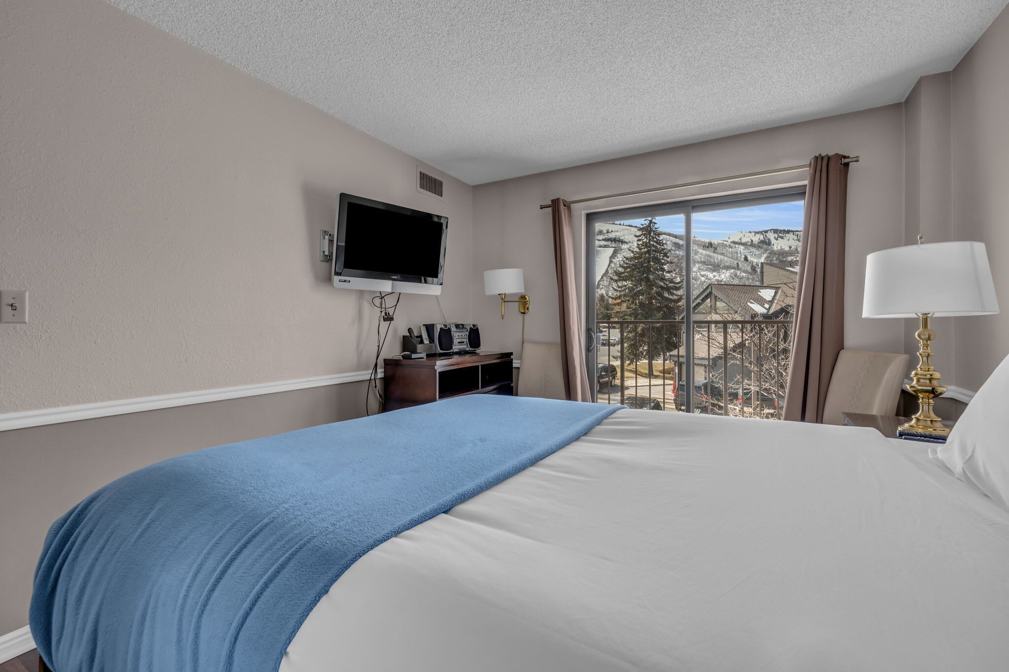 Een hotelkamer met een groot bed, een aan de muur bevestigde televisie, een bureau met een computer en uitzicht op een besneeerd landschap.