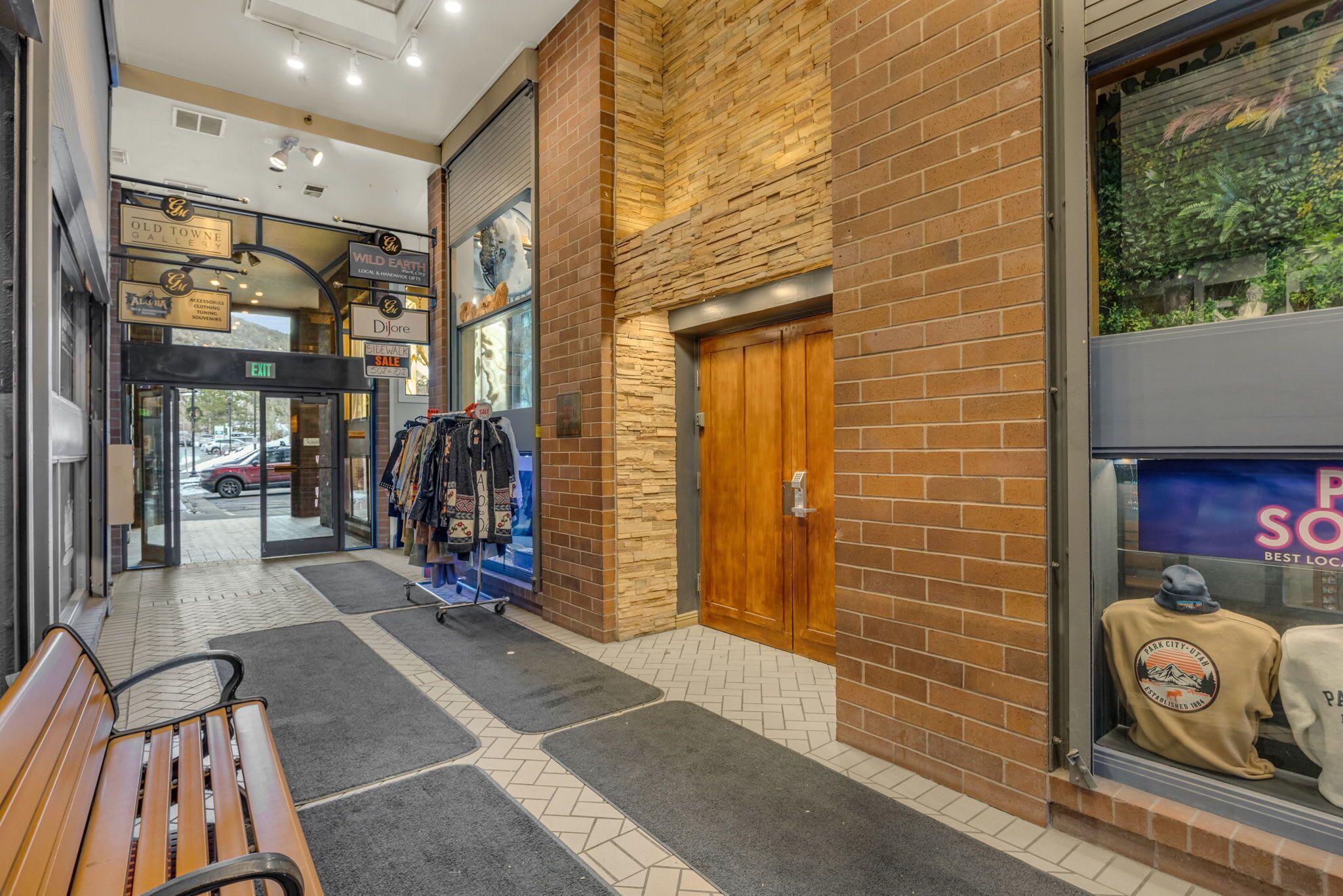 A brick building with a wooden door, a bench, and a display window with a hat.