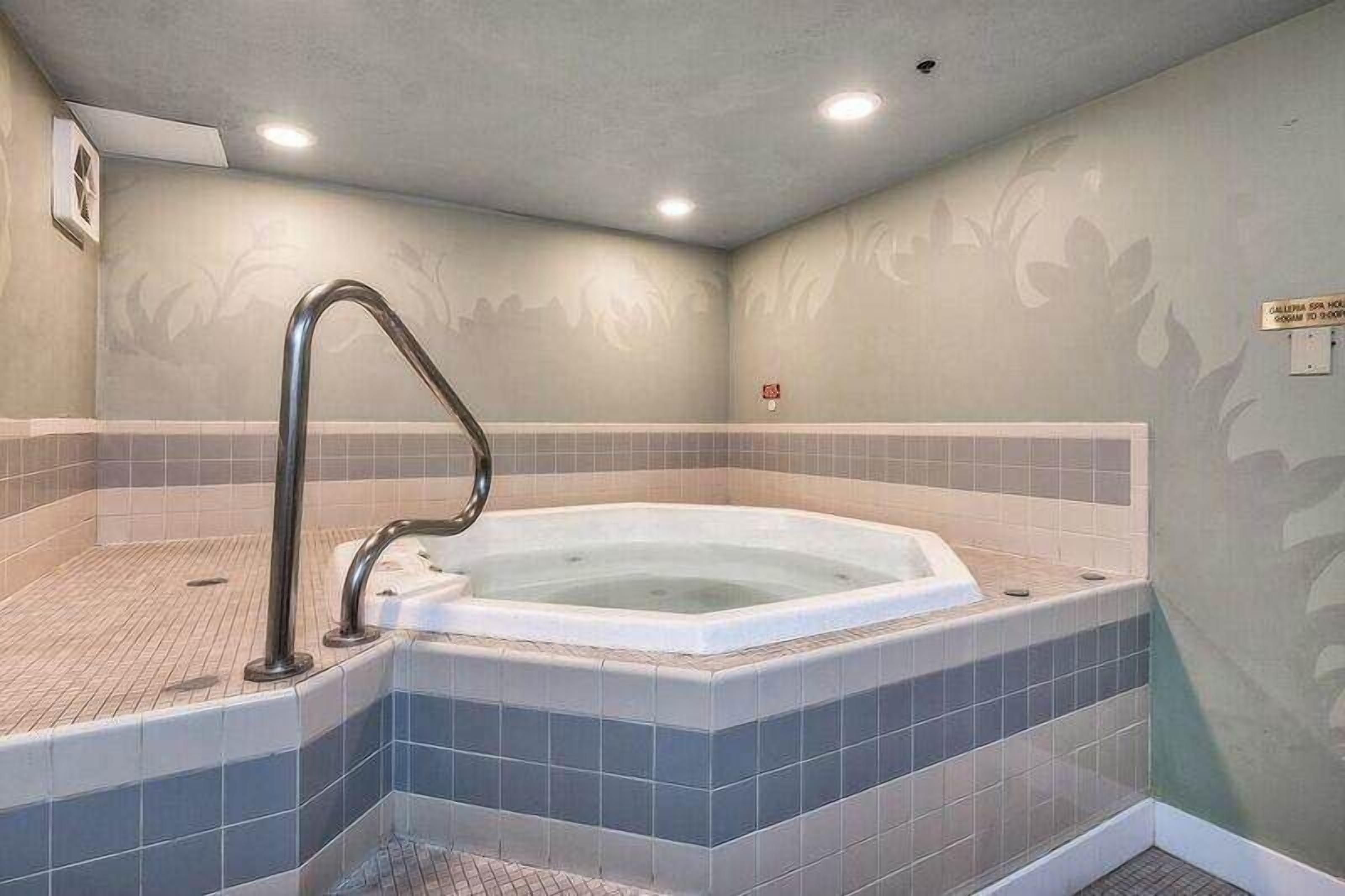 Un cuarto de spa con un jacuzzi, paredes con azulejos y un pasamanos.