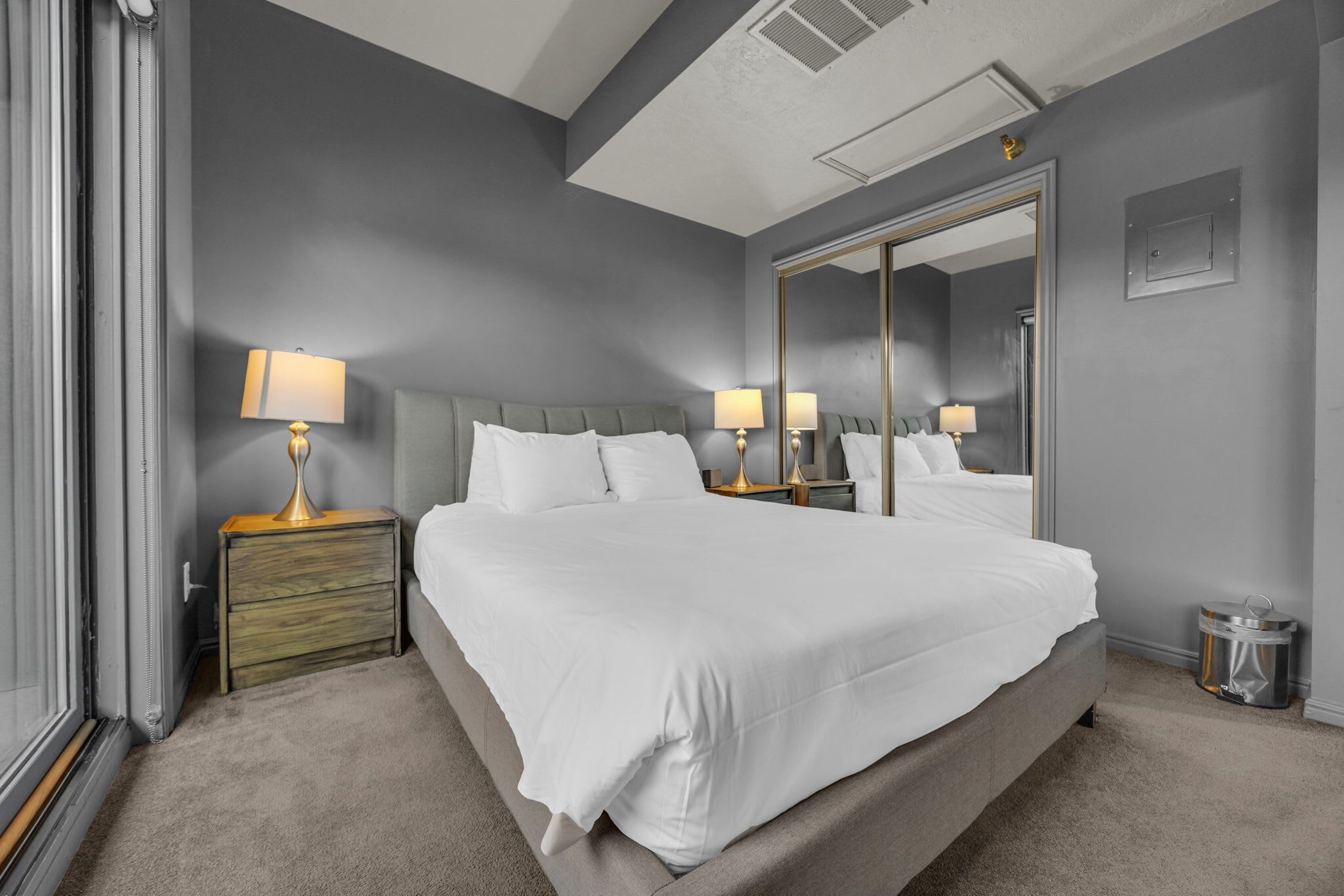A hotel room with a large bed, two bedside tables with lamps, a mirror, and a trash can.