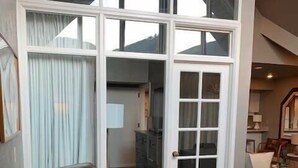Ein großzügiger Wohnbereich mit braunem Ledersofa und Fußhocker, eine große Schiebetür zum Balkon und eine moderne Küche im Hintergrund.