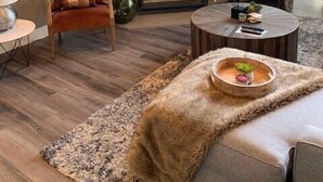 Ein modernes Wohnzimmer mit Kamin, einem darüber montierten Fernseher und einer gemütlichen Sitzecke mit Teppich und einer Schale Obst.