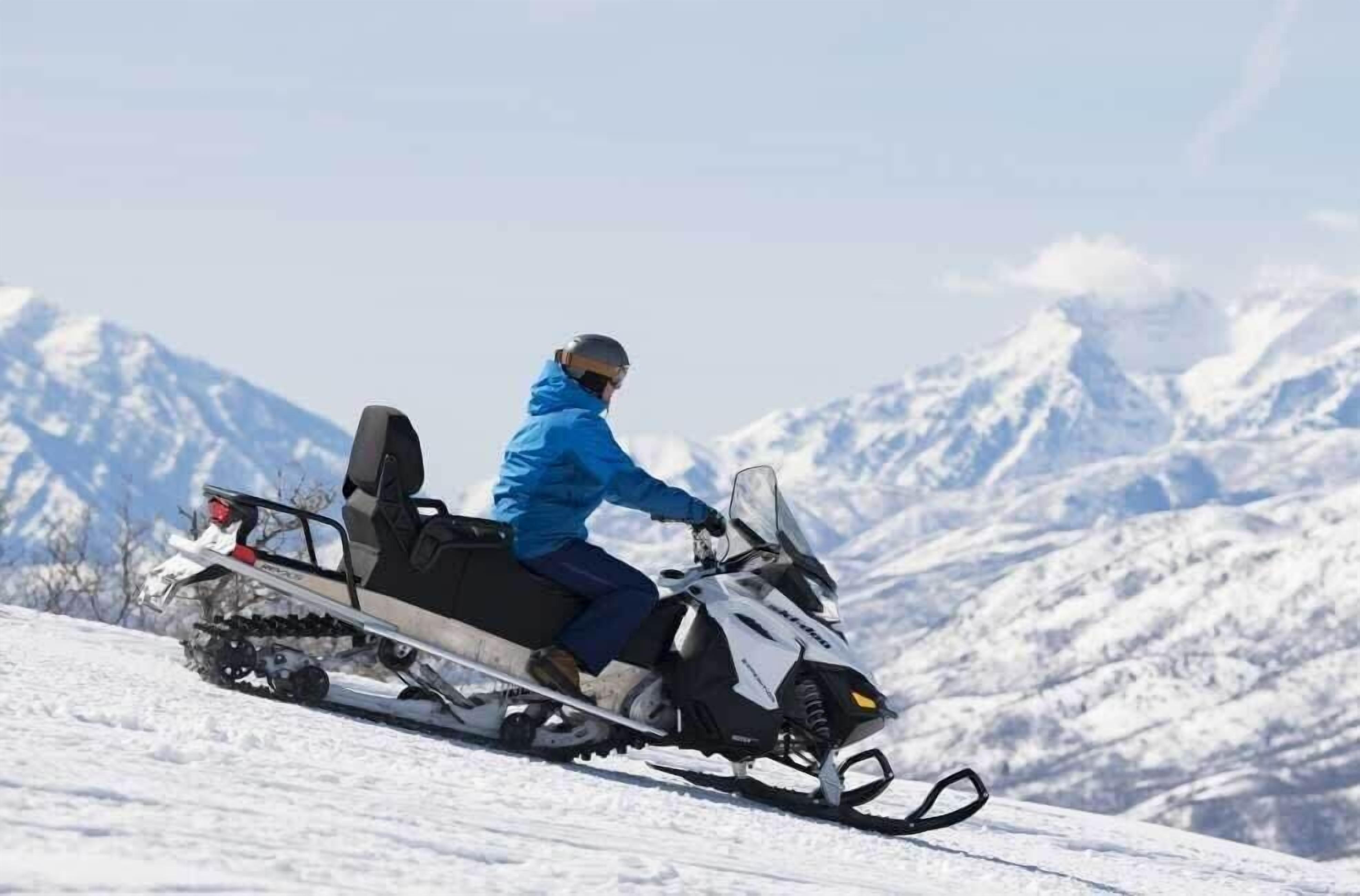A person riding a snowmobile on a snowy slope with mountains in the background.