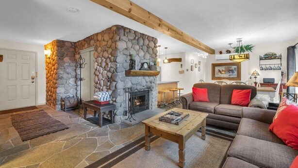 A cozy living room with a stone fireplace, wooden beams, a sofa, and a coffee table.