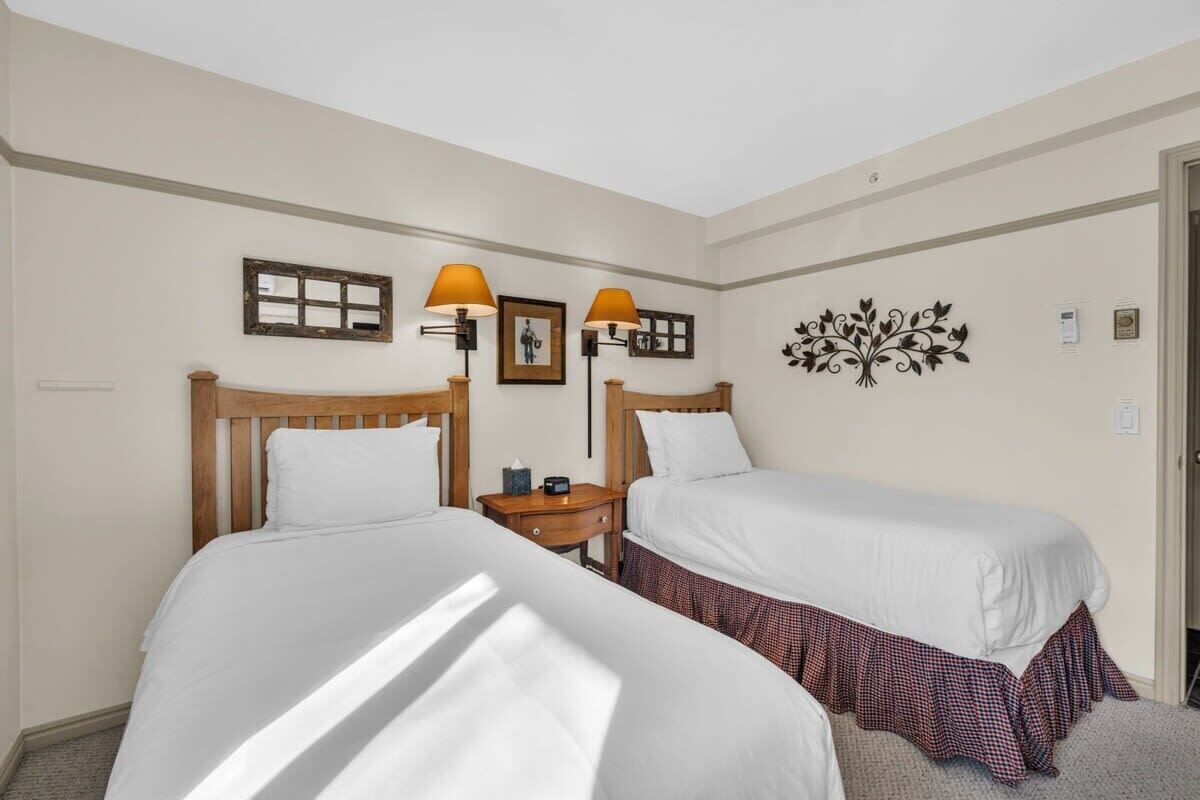 Une chambre d’hôtel avec deux lits, une tête de lit en bois, une table de chevet avec une lampe et un élément décoratif mural.