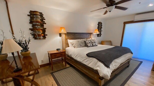 A bedroom with a wooden bed, two bedside lamps, a ceiling fan, and a large window.