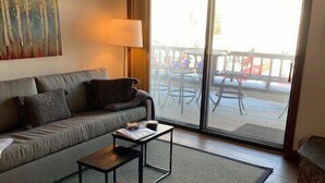 A living room with a sofa, a coffee table, a lamp, and a view of an outdoor deck through a sliding glass door.