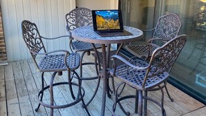 A patio with a round table and four chairs, a laptop on the table, and a sliding glass door in the background.
