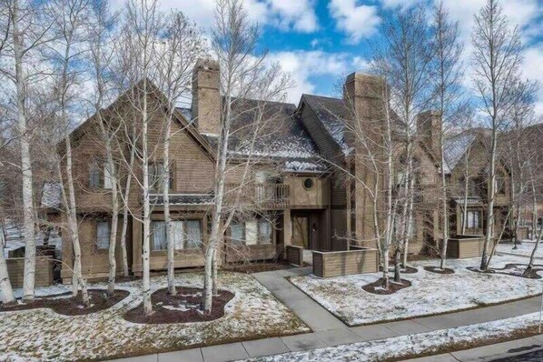 A large, rustic-style house with a prominent chimney, surrounded by a snow-covered landscape and bare trees.