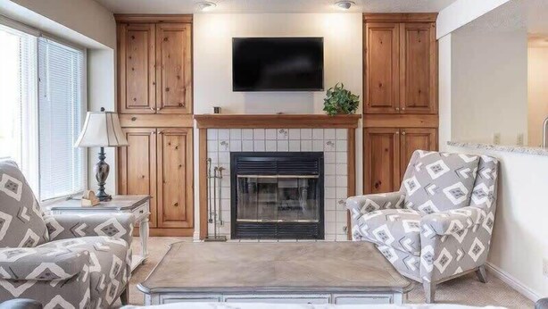 A living room with a fireplace, wooden cabinets, a television, and patterned furniture. - Charming 2 BDR Getaway w/ Views & Private Hot Tub! (Park City)