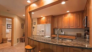 A kitchen with wooden cabinets, a granite countertop, a sink, and a refrigerator. - Ski-in/out 2 BDR Condo in the Heart of the Action! (Park City)