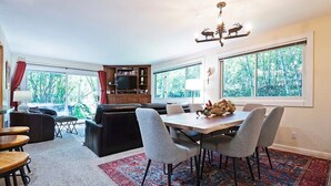 A modern living room with a dining area, large windows, a fireplace, and a television. - Ski-in/out 2 BDR Condo in the Heart of the Action! (Park City)