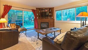A living room with a fireplace, leather furniture, and large windows with a forest view. - Ski-in/out 2 BDR Condo in the Heart of the Action! (Park City)