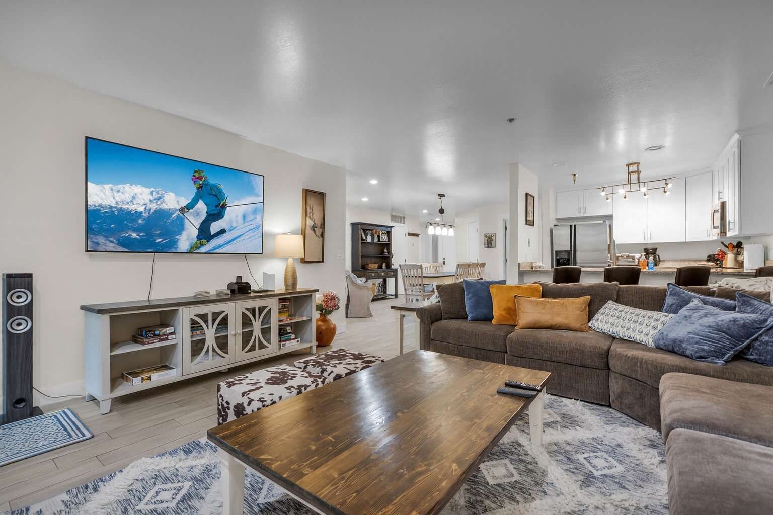 Una sala de estar moderna con un televisor de pantalla plana grande, una mesa de centro de madera y un sofá con varios cojines.
