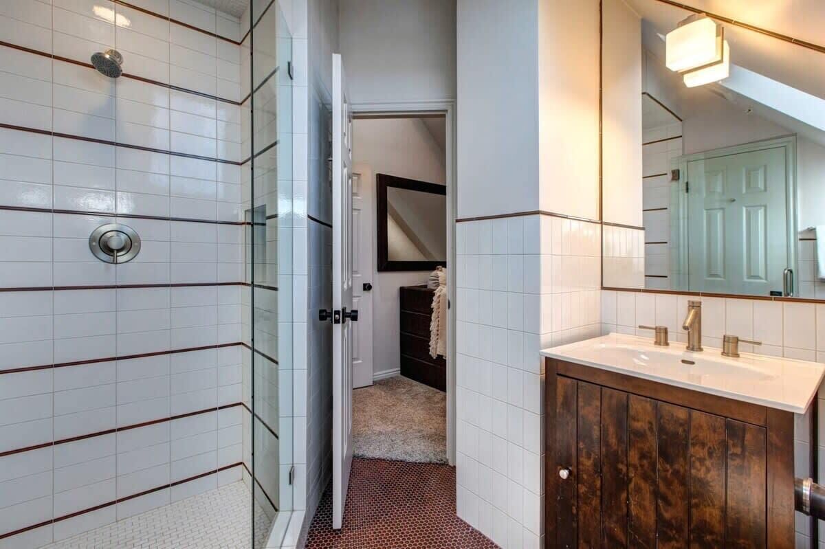 A bathroom with white tiled walls, a wooden vanity, and a mirror.