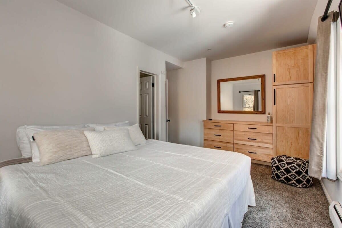 A bedroom with a large bed, a wooden wardrobe, and a mirror on the wall.