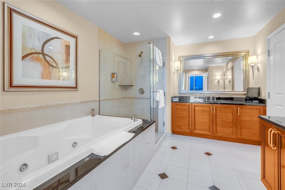 A modern bathroom with a large bathtub, a glass-enclosed shower, wooden cabinets, and a large mirror.