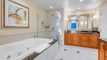 A modern bathroom with a large bathtub, a glass-enclosed shower, wooden cabinets, and a large mirror.