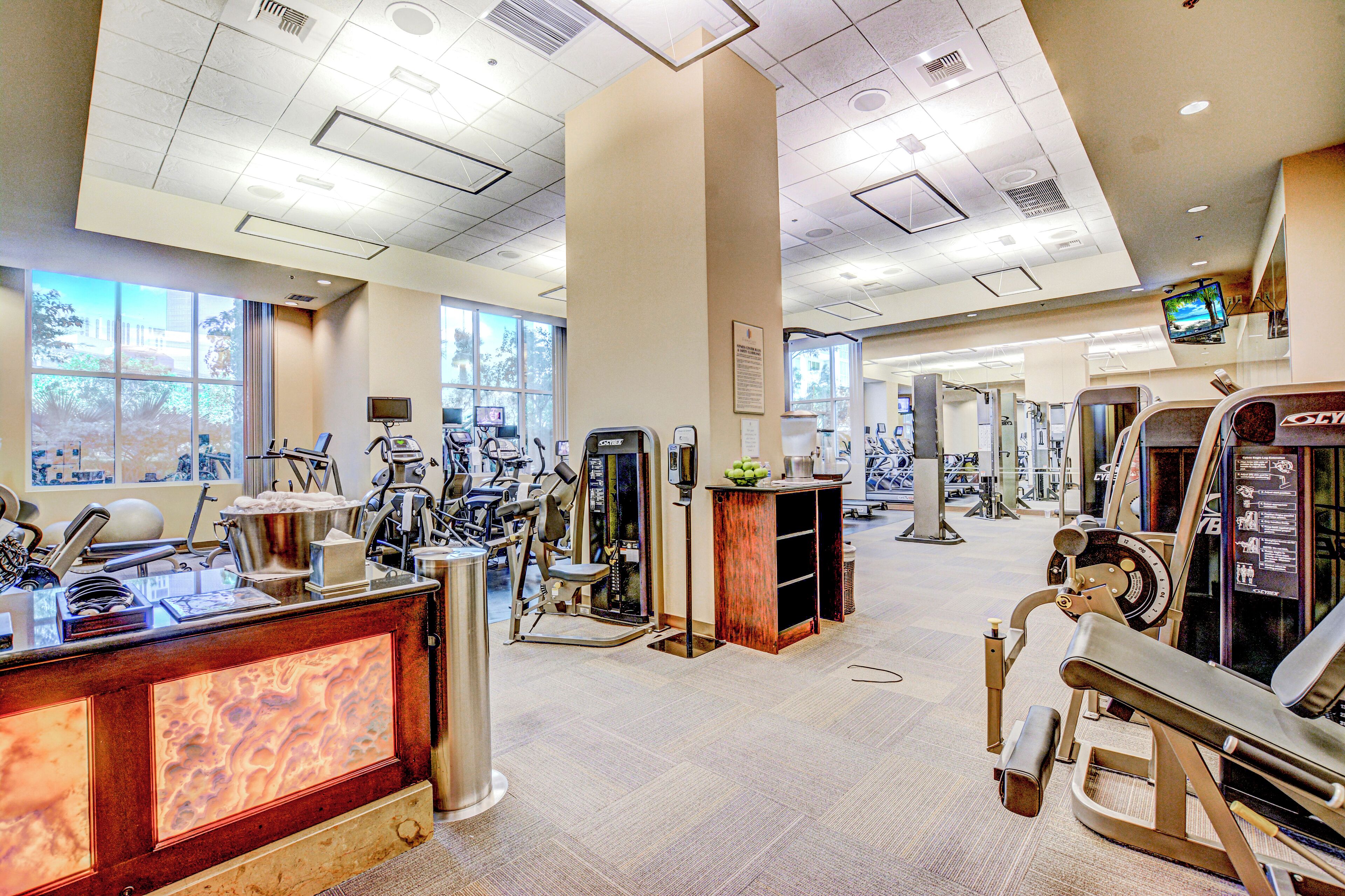 A gym with various exercise machines, a reception desk, and large windows.