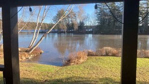 A view through a window of a building with a pond in the foreground and trees in the background. - Whitney Landing: A Lakeside Getaway on Upper Cold Stream Pond (Lincoln)