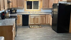 A compact kitchen with wooden cabinets, a black refrigerator, and a microwave. - Whitney Landing: A Lakeside Getaway on Upper Cold Stream Pond (Lincoln)