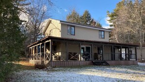 A two-story house with a porch, a covered area, and a small front yard with snow. - Whitney Landing: A Lakeside Getaway on Upper Cold Stream Pond (Lincoln)