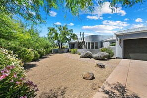 A residential property with a gravel driveway, a garage, and a landscaped garden with various shrubs and flowering plants. - Serenity Peaks- Gorgeous Pet Friendly Villa in Scottsdale with Pool, Spa, and Bikes (Scottsdale)