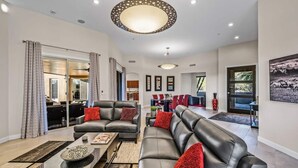Un salon spacieux avec un canapé en cuir noir, une table basse et un coin repas avec des chaises rouges.