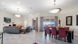 Un salon spacieux avec un canapé gris, une table à manger avec des chaises rouges et une grande fenêtre avec des rideaux.