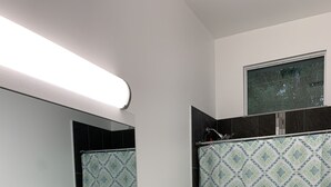 Un baño moderno con lavamanos, espejo y retrete blancos. Hay una cortina de ducha con un estampado geométrico y una alfombra azul y blanca en el suelo.