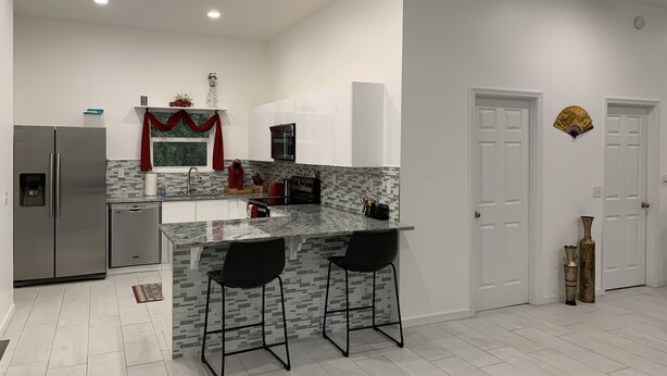 Una cocina moderna con una isla central, dos taburetes de bar, un refrigerador, un microondas y un lavamanos.