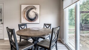 A dining area with a round table, six chairs, a chandelier, and a large abstract painting on the wall. - Cozy Home in Downtown Fishers (Fishers)