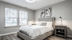 A bedroom with a large bed, two bedside tables, and a window with blinds. - Cozy Home in Downtown Fishers (Fishers)