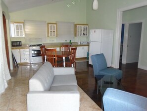 Ein Wohnzimmer mit einer Couch und einem blauen Sessel, ein Essbereich mit Tisch und Stühlen sowie eine Küche mit Geräten und Schränken.